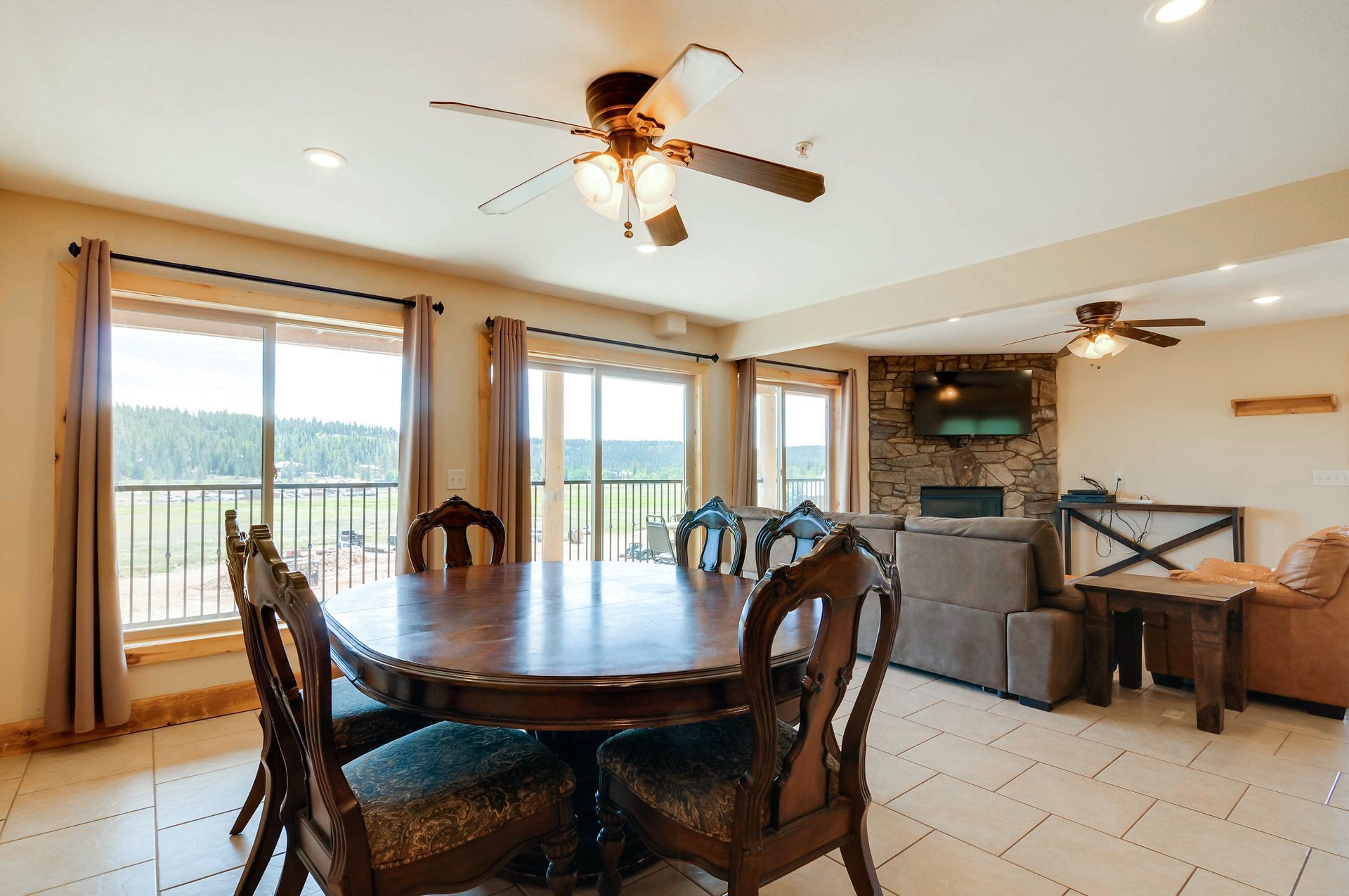 Dining area with a large wooden table and chairs, with views of a natural landscape through large windows.