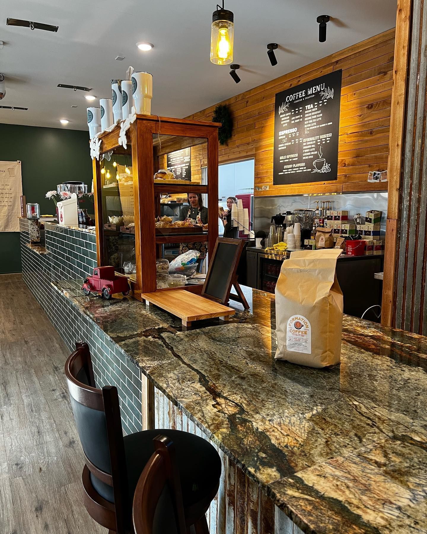 Coffee shop interior: counter with granite top, bar stools, coffee bag, baked goods display, and menu board.