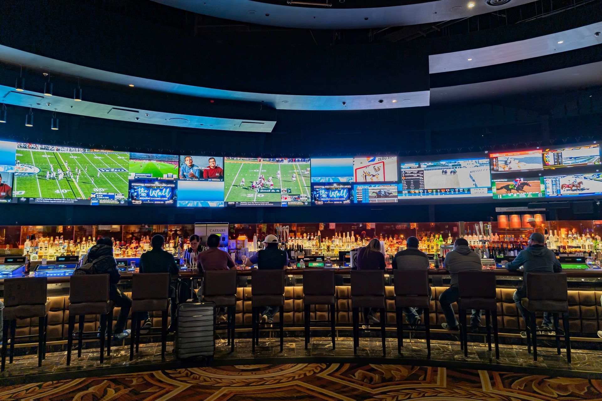 A group of people are sitting at a bar in front of a large screen.