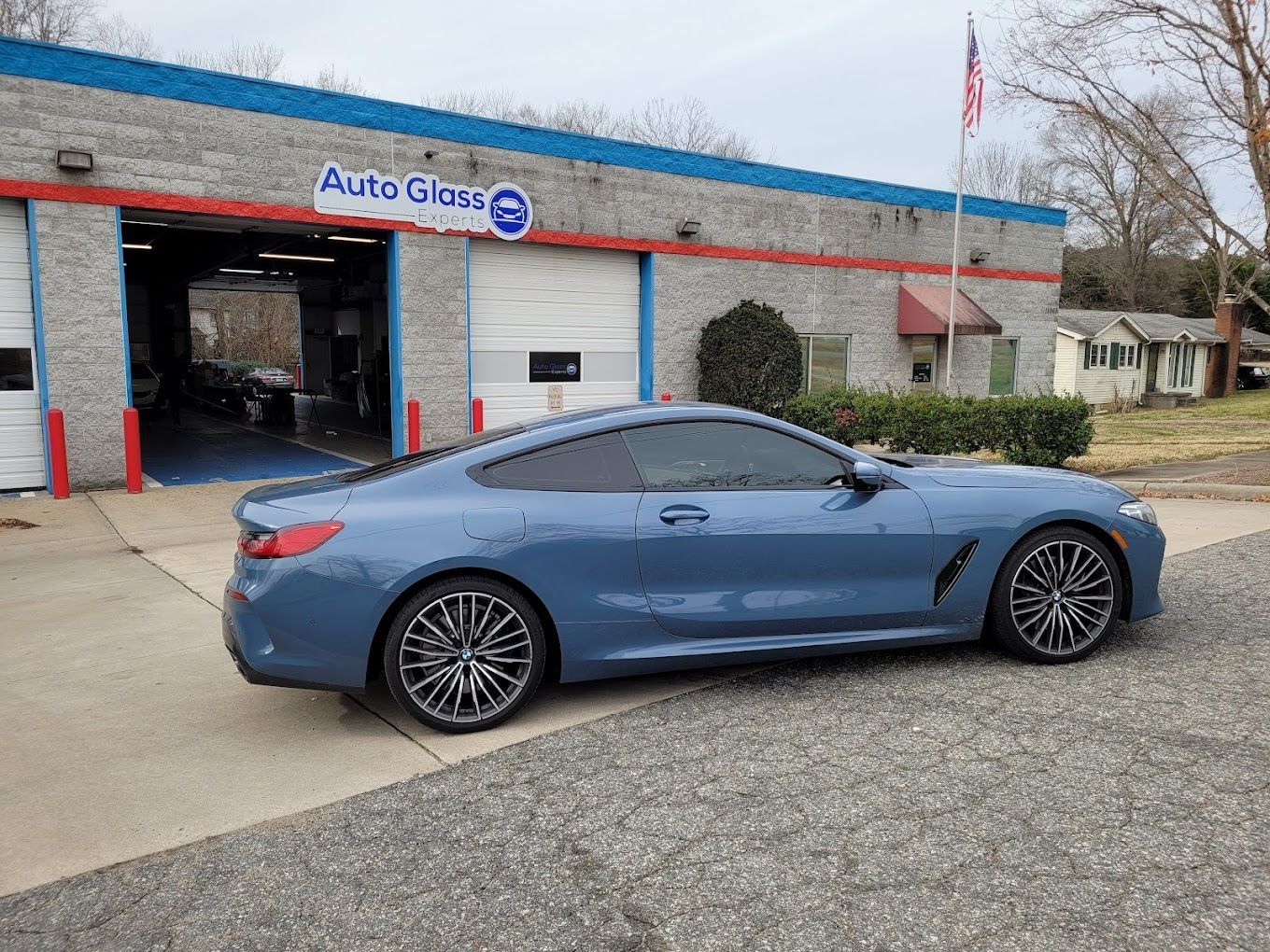Blue sports coupe parked outside an auto glass shop, viewed from the side.