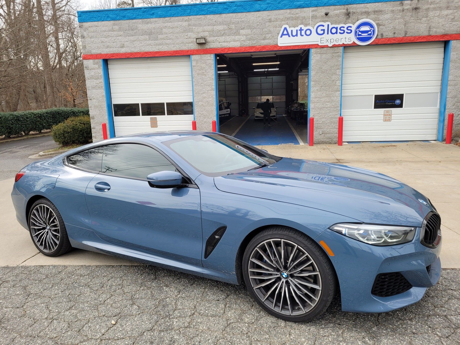Blue sports coupe parked outside an auto glass shop