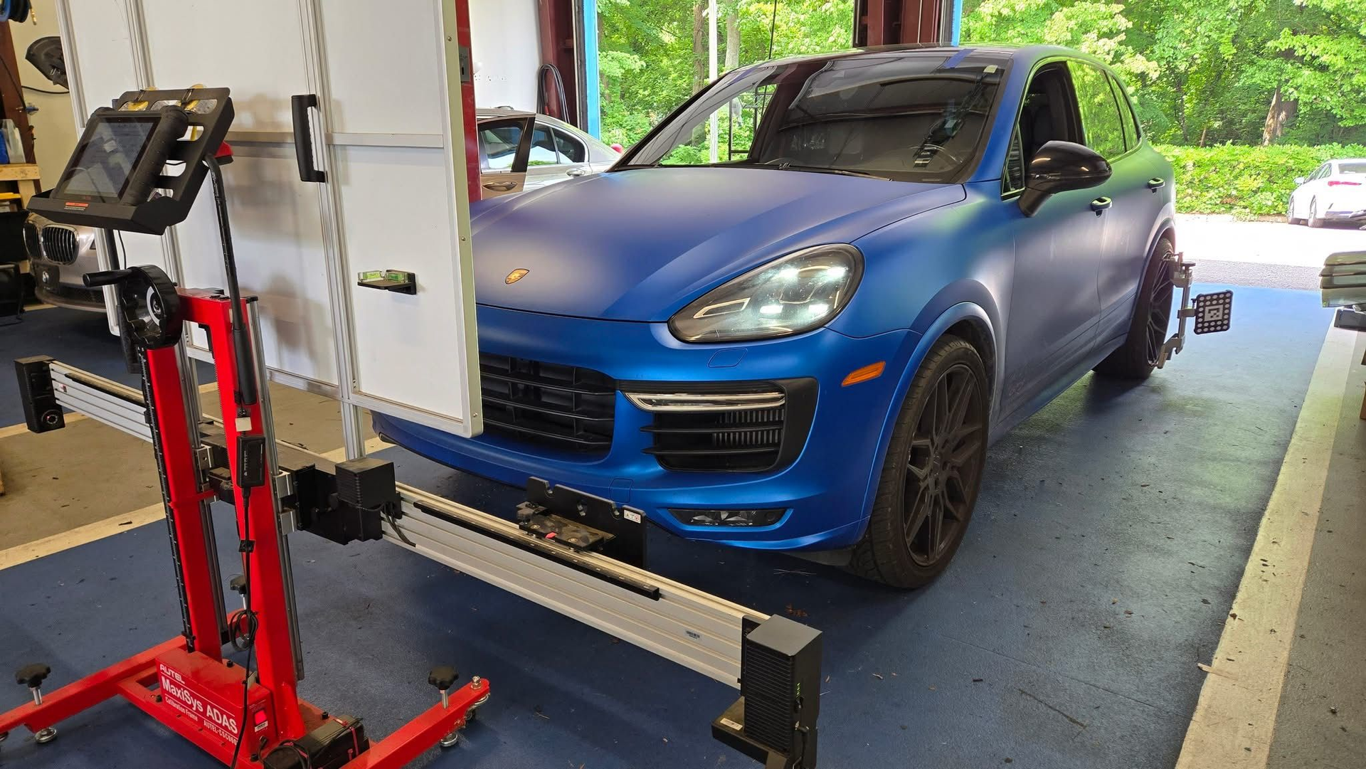 Blue SUV on a lift in an auto shop, with a red floor jack and workbench nearby