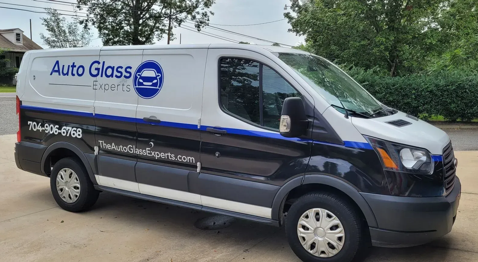 White Auto Glass service van parked outdoors on a gravel lot, with blue stripes and logo on the side