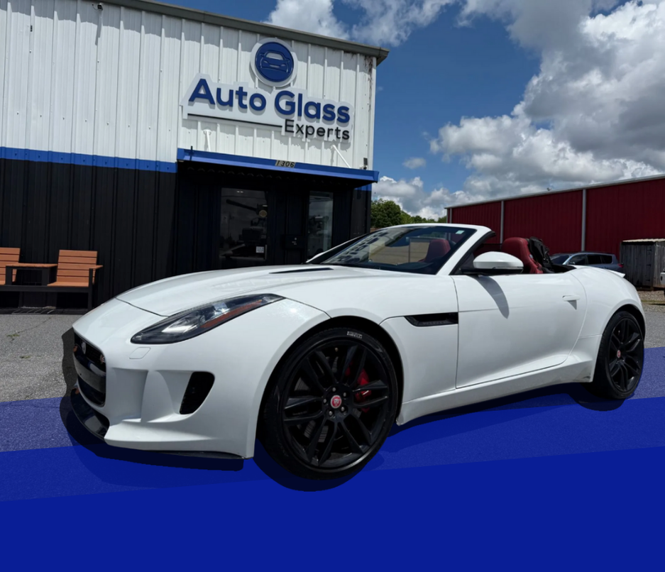 White convertible sports car parked outside an Auto Glass Experts shop under a blue sky.