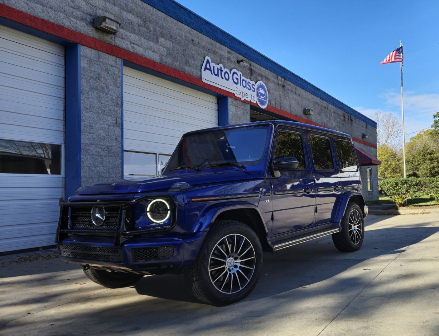 Dark blue Mercedes G-Class SUV parked outside an AutoGuru shop on a sunny day