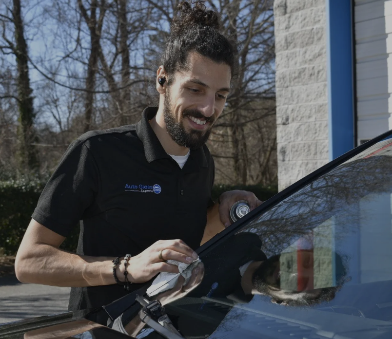 Man polishing a car windshield outdoors beside a building on a sunny day