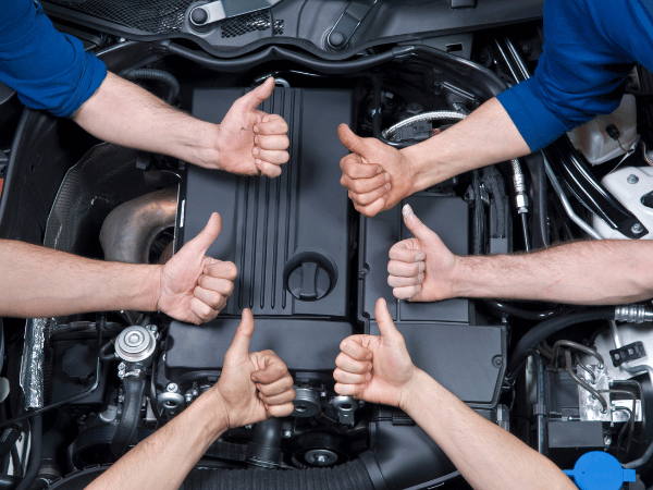 Mechanics giving thumbs up around a car engine in the open hood compartment