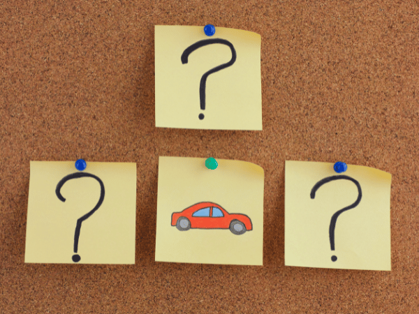 Three sticky notes with question marks around a central sticky note showing a red car on a corkboard.
