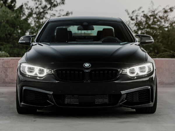 Front view of a black BMW sedan with headlights on, parked outdoors.