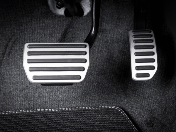 Car pedals in a car interior: brake and accelerator with black rubber grips on dark carpeting