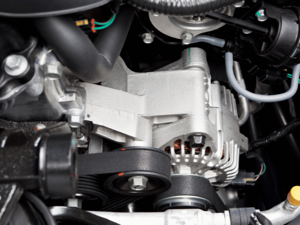 Close-up of a car engine’s alternator and belts with silver and black components