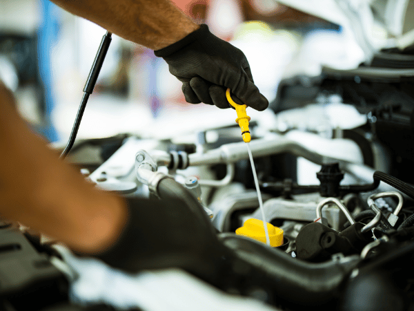 Mechanic checking engine oil with a yellow dipstick in an open car engine bay