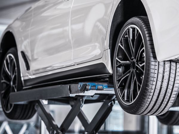 White car lifted on a scissor jack in a garage, front wheel raised for repair