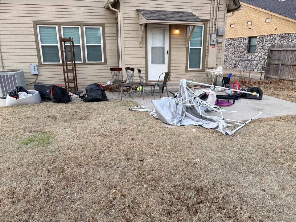 Front yard with scattered yard waste, tarps, bags, and tools in front of a house.
