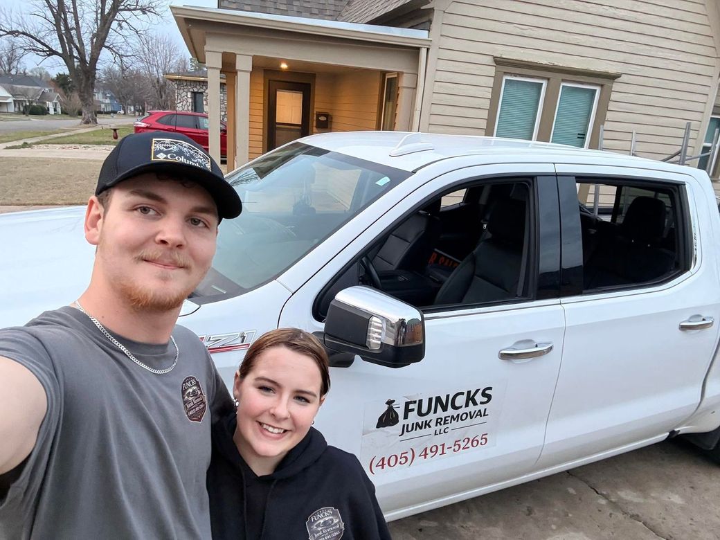 Two smiling people pose beside a white Funcks Service truck in a driveway at dusk.