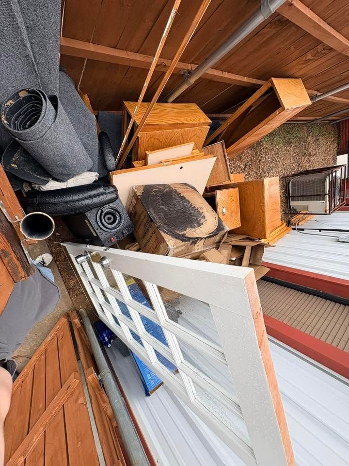 Rotated view of a cluttered storage area with furniture, rolled rugs, and a white door panel.