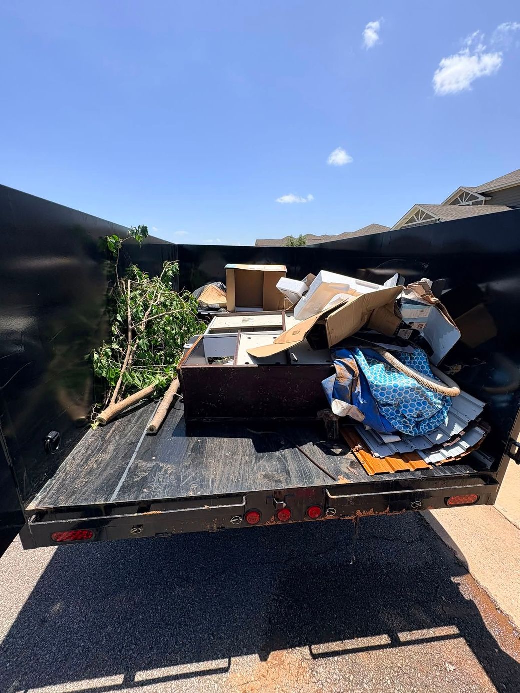 Pickup truck bed piled with boxes, cardboard, and blue bags in a sunny driveway
