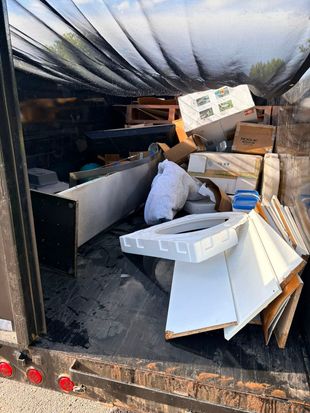 Cluttered moving trailer packed with boxes, furniture, and loose items under a black tarp.