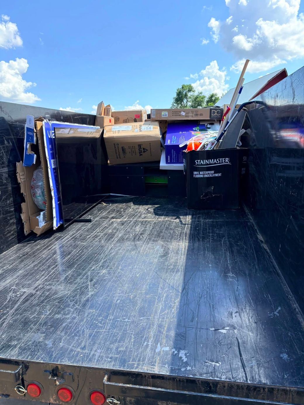 Dumpster bed with black liner and cardboard boxes under a bright blue sky.