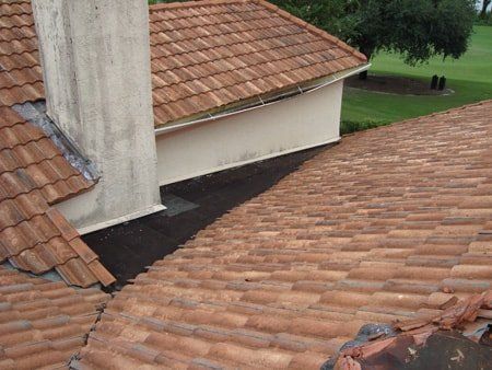 Clay tile roof with chimney and a flat, dark roof section.