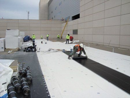 Construction workers installing roofing materials on a building rooftop. White insulation and black membrane.