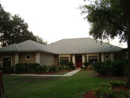 Beige ranch-style house with gray roof, red front door, and green lawn.