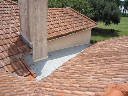 Clay tile roof with chimney, close-up. Shows flashing, building edges, and a golf course in the distance.