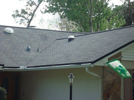 Gray shingled roof with multiple vents and black trim. White siding below with a green flag.