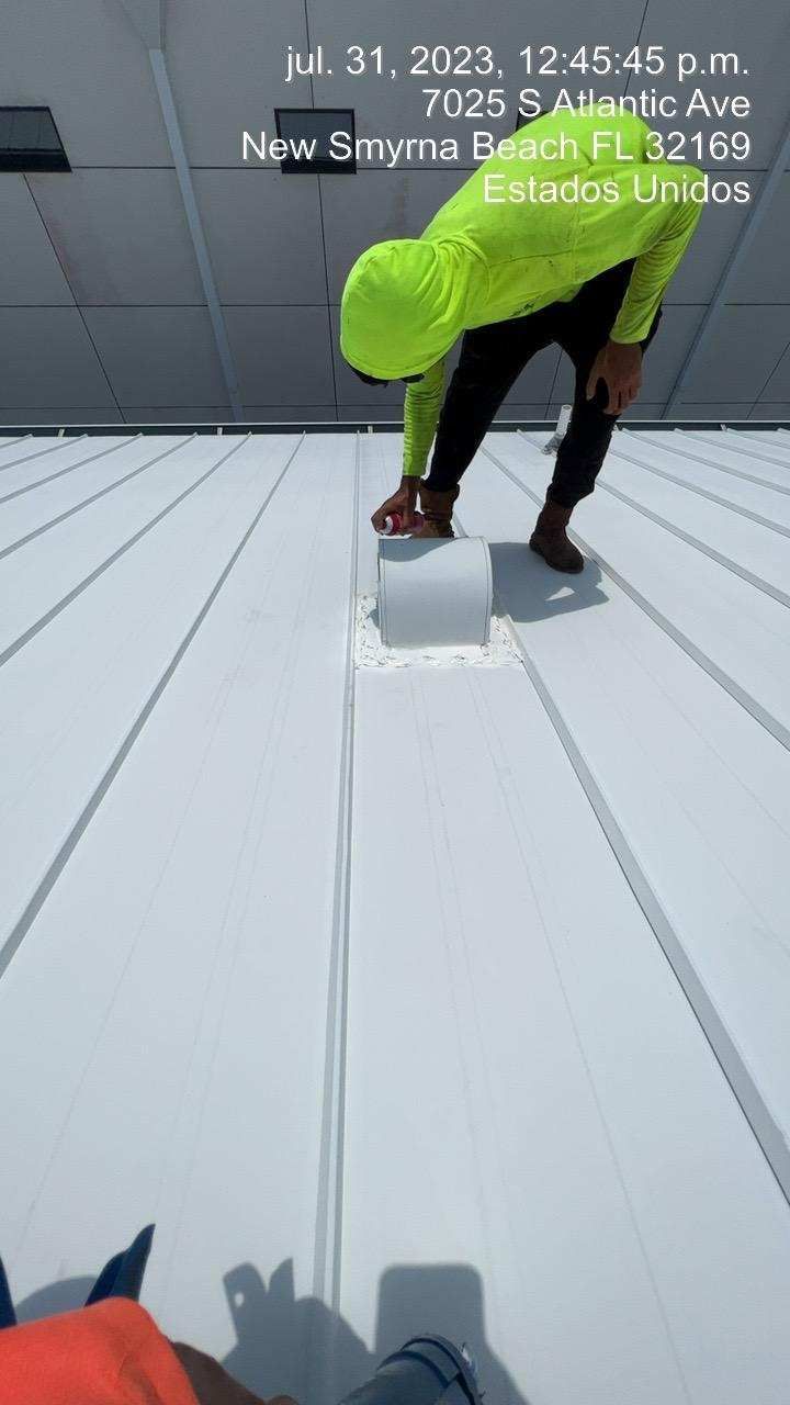 Person on a white roof, examining a vent. Yellow shirt, black pants. Location: Florida, USA.
