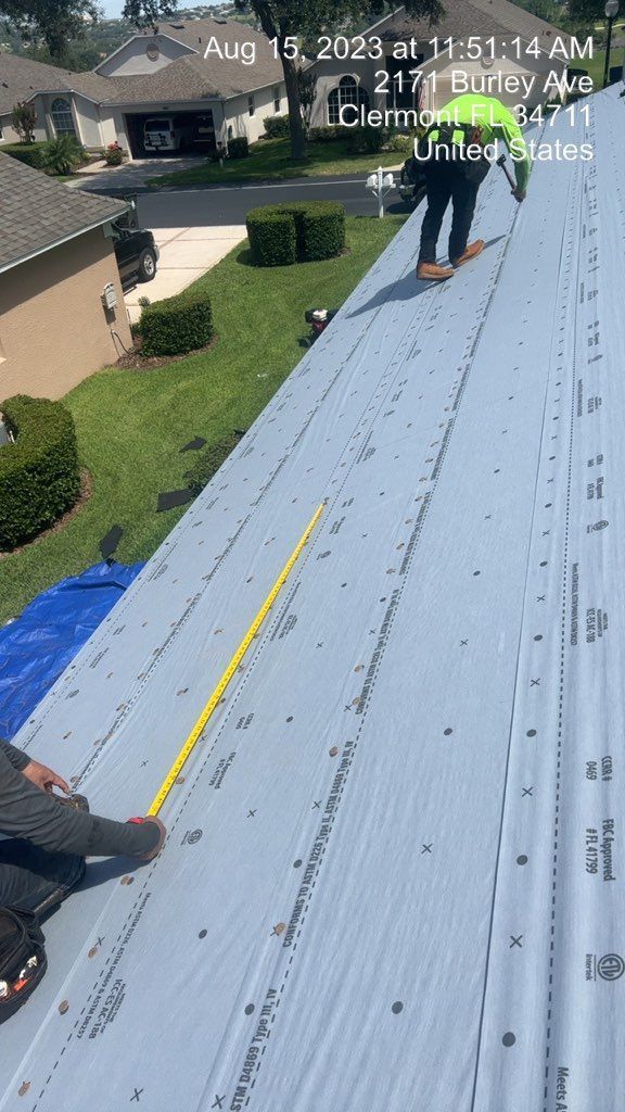 Two workers on a metal roof measure with a tape measure on a sunny day.
