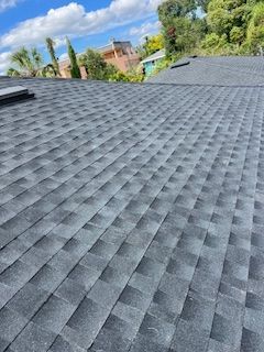 Dark gray asphalt shingle roof on a building, with a cloudy blue sky in the background.