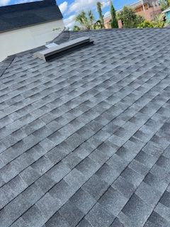 Gray asphalt shingle roof on a residential building with a skylight and a sunny sky background.