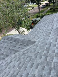 Gray asphalt shingle roof, angled view; tree and suburban street visible in background.