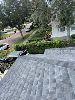 View of a gray shingle roof and street with cars, trees, and a house with white siding.