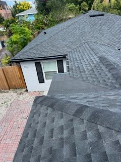 A house with a newly shingled roof, black shingles. A wooden fence is on the left.