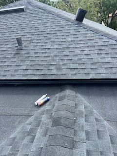 Roof with dark gray shingles, two vent pipes, and tubes of sealant.