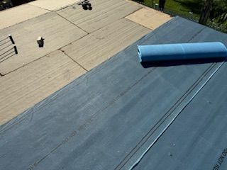 Flat roof construction showing gray underlayment and rolled blue material. Beige insulation is also present.