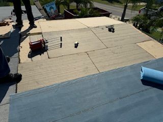 Roofers working on a roof, preparing for new shingles. Plywood on deck, tools, blue tarp.