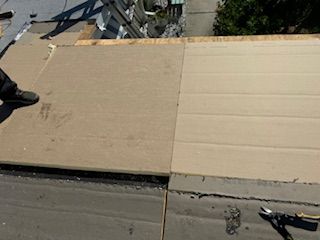 Roofing materials being installed on a roof; plywood and dark asphalt visible.