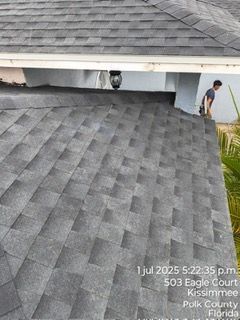 Roofer working on a gray shingled roof next to a white overhang. Kissimmee, Florida.