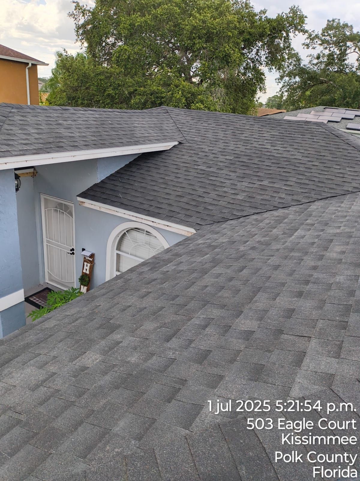 Dark gray shingle roof of a light blue house. Green trees in background. Kissimmee, Florida.