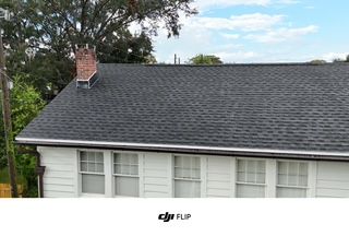 Gray shingled roof on a white house with a chimney. Blue sky in background.