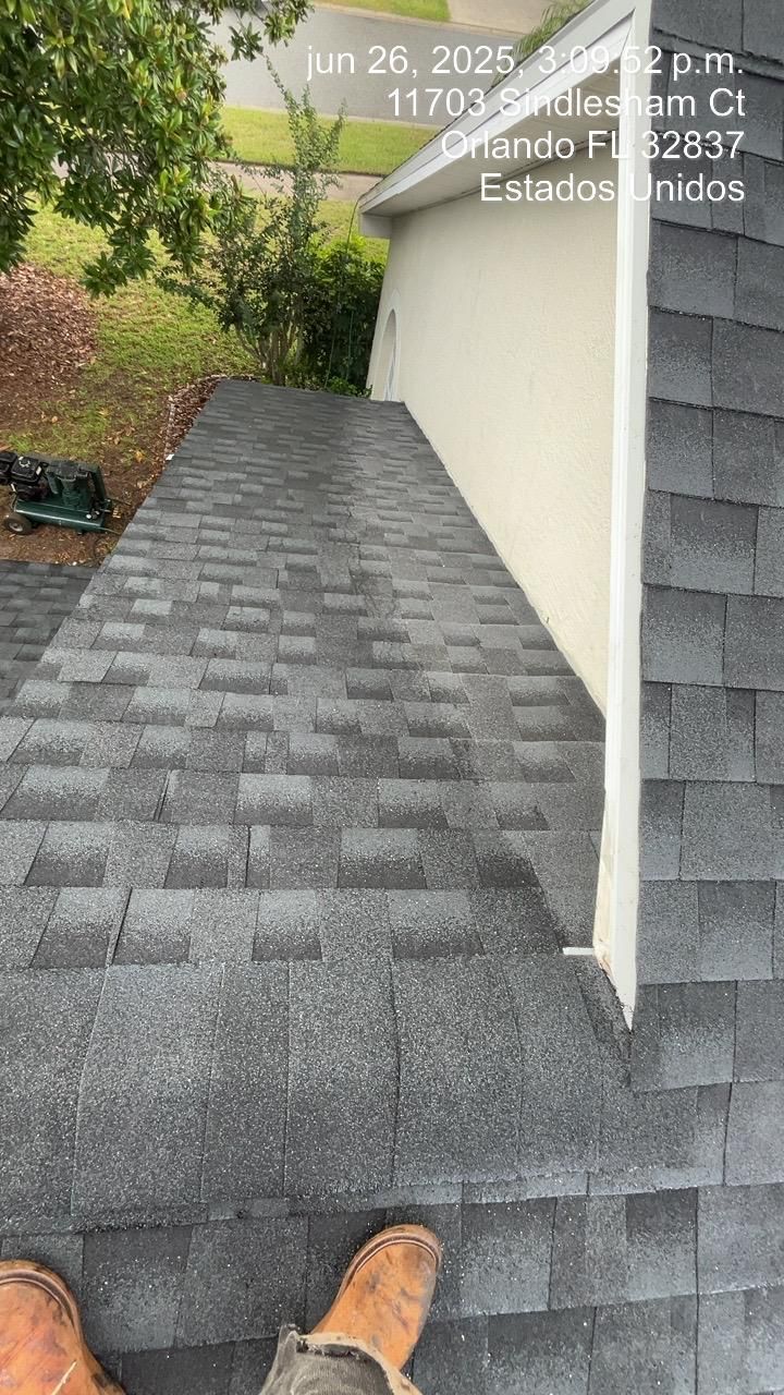 Person standing on a dark shingle roof next to a white wall. Date/location stamp visible.