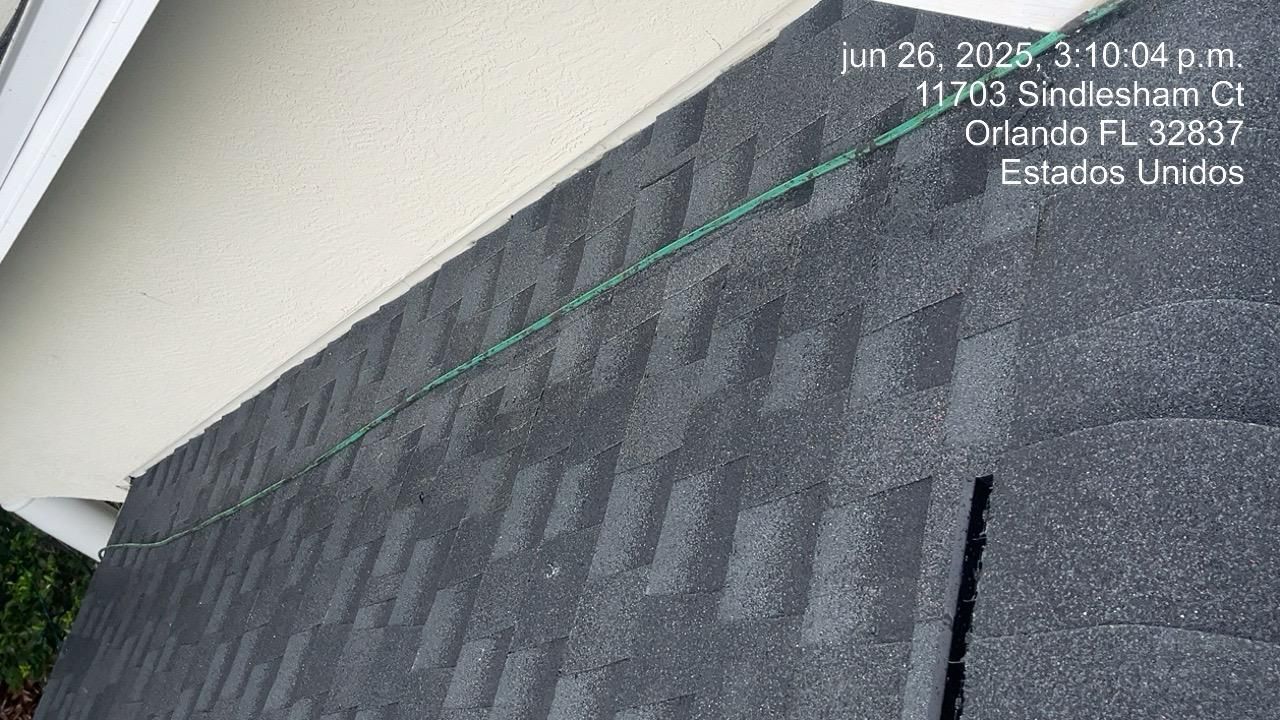 Close-up of a dark asphalt shingle roof, with the date and address visible.