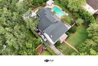 Aerial view of a white house with a dark roof, pool, and green yard, surrounded by trees.