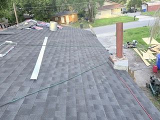 A roof under construction; gray shingles, metal flashing, and a brick chimney visible.