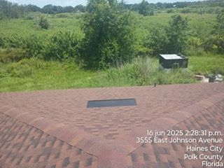 Brown shingle roof with a rectangular vent, overlooking a grassy field. Haines City, Florida.