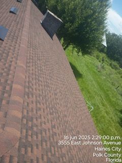 Roof of a building with brown shingles, near green grass and trees. Date and address are visible.