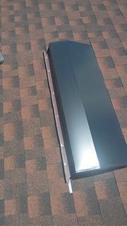 Dark metallic car part on a brown and red shingle roof.