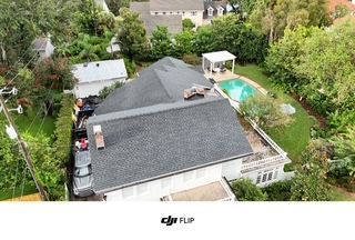 Aerial view of a house with a dark roof, pool, and surrounding trees.